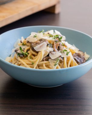 creamy pasta dish topped with savory mushroom sauce, grated parmesan, and fresh thyme, served in a blue bowl
