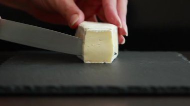 Kadınlar ellerini dikkatlice koyu bir zeminde yumuşak brie peynirini dilimliyor.