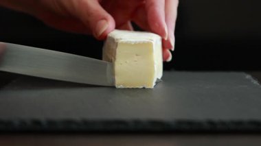 Kadınlar ellerini dikkatlice koyu bir zeminde yumuşak brie peynirini dilimliyor.