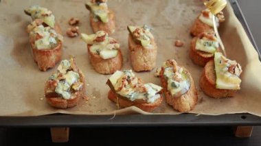 Elleri kremalı, mavi peynirli ve taze armut dilimli crostini hazırlıyor.