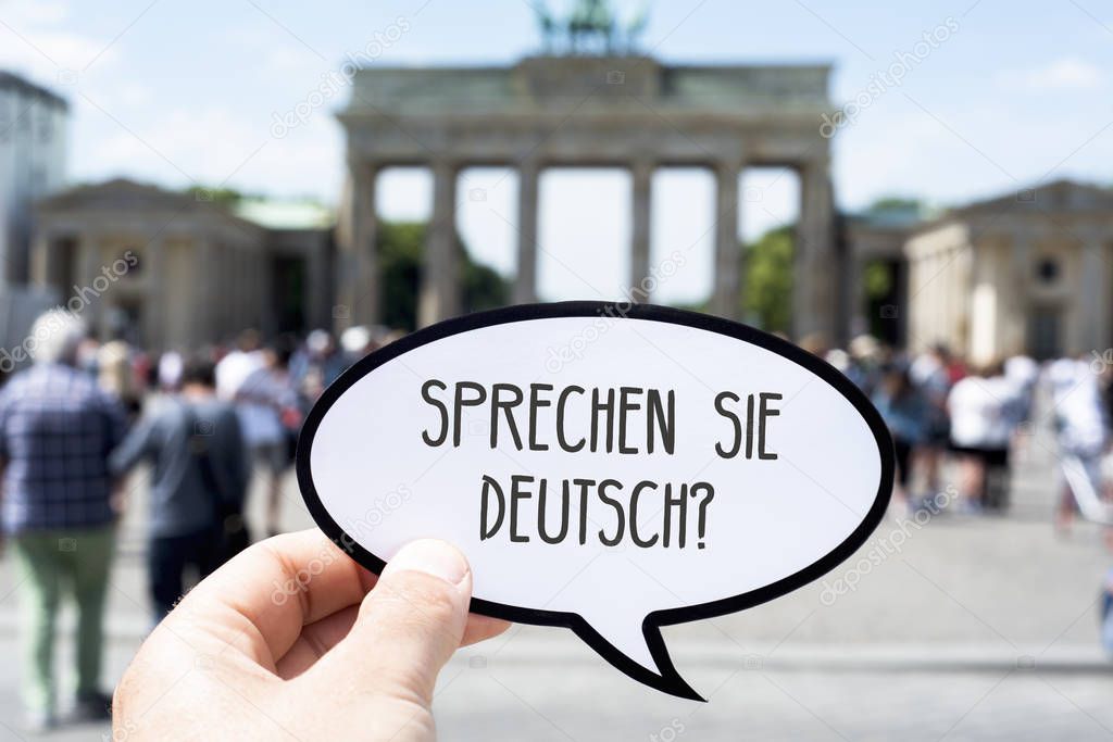closeup of the hand of a young caucasian man showing a speech bubble with the question sprechen sie deutsch, do you speak german written in german, in front of the Brandenburg Gate in Berlin, Germany