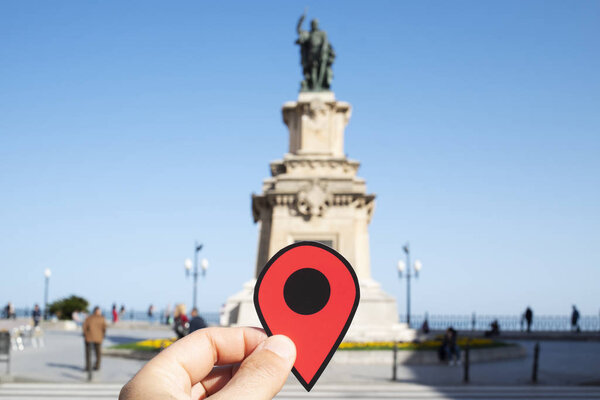 the hand of a young caucasian man with a red marker at the end of the popular Rambla Nova street, in Tarragona, Spain, highlighting the monument to Roger de Lluria and the Mediterranean Balcony