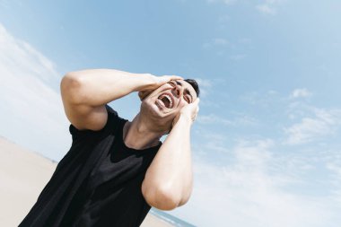 closeup of a suffering caucasian man outdoors, screaming with his hand in his head clipart