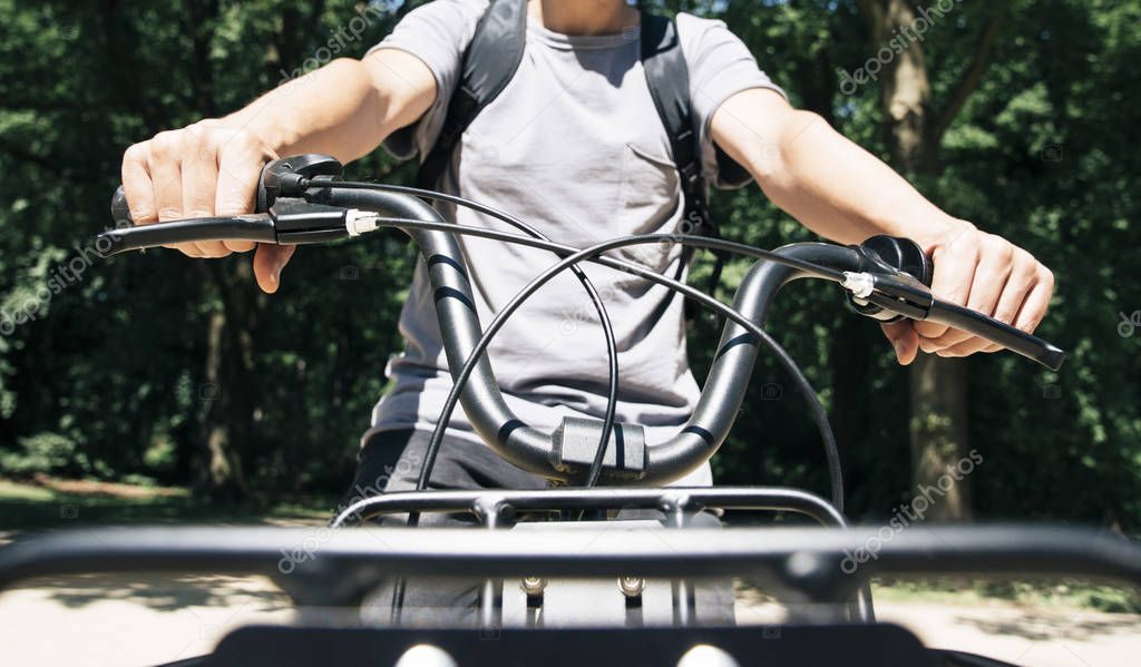 closeup of a young caucasian man, carrying a backpack, seen from the front, riding a bike by a public park