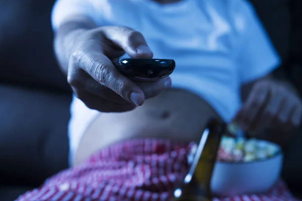 一个高加索男人在内衣 啤酒肚 坐在沙发上 喝啤酒 吃爆米花 而看电视 — 图库照片