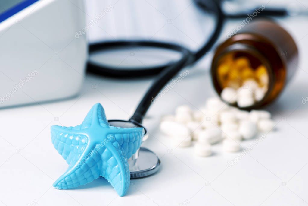 closeup of a blue plastic starfish and some pills on a doctors desk, in a doctors office, depicting the medical assistance in summer