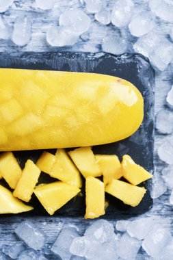 high anble shot of a homemade ice pop made with natural pineapple or mango, on a natural slate tray surrounded by ice clipart