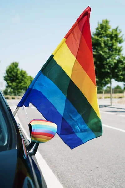 closeup of a rainbow flag in the wing mirror of a car and another rainbow flag popping up from the window