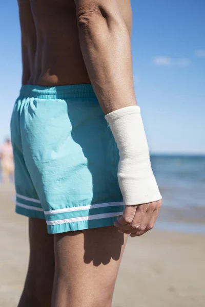 海を前に 彼の手首に包帯を巻くとビーチで水着で若い白人男のクローズ アップ — ストック写真