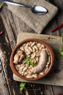 high-angle shot of an earthenware bowl with a cassoulet de Castelnaudary, a typical bean stew from Occitanie, in France, on a rustic wooden table clipart