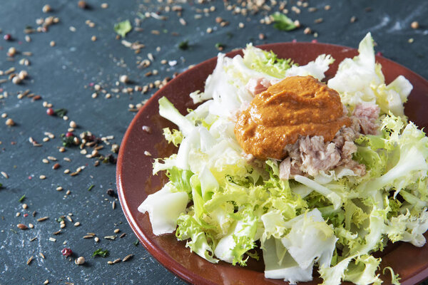 escarola amb romesco, escarole endive with romesco sauce, a typical salad from Catalonia, Spain, on a brown earthenware plate, placed on a rustic dark wooden table