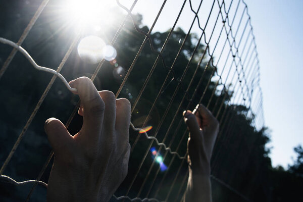 closeup of the hands of a man trying to climb up a metal fence