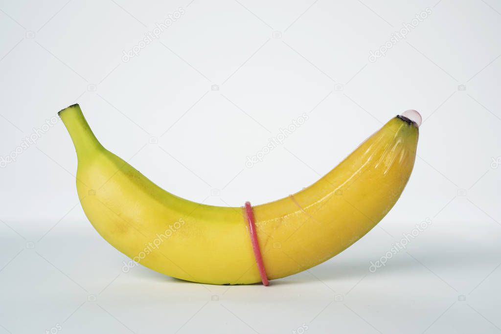 closeup of a banana with a pink condom in it on an off-white background