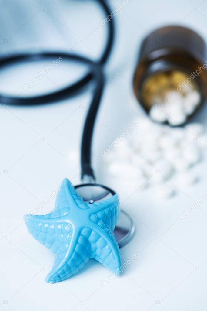 closeup of a blue plastic starfish and some pills on a doctors desk, in a doctors office, depicting the medical assistance in summer