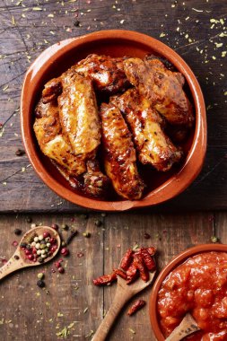 Barbekü tavuk kanadı bir toprak plaka ve barbekü sosu ile bir kase içinde yüksek açılı görünüş bir rustik ahşap tablo