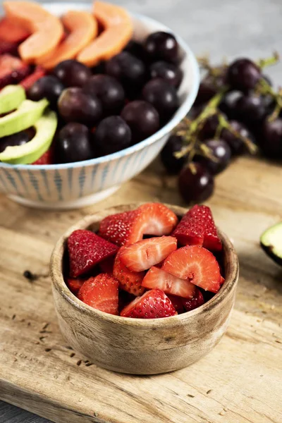bazı çilek ile şimşir kase ve bir meyve salatası ile seramik kase closeup yapılan avokado, papaya, çilek, üzüm ve ahşap bir masa üzerinde bir kesme tahtası üzerinde yaban mersini