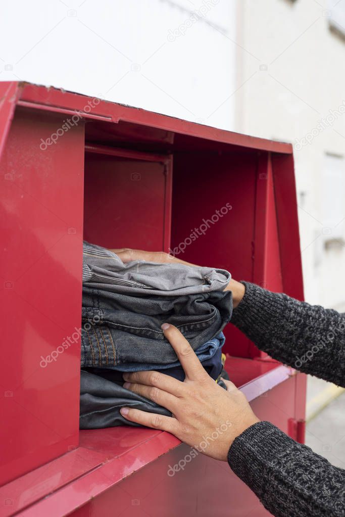 closeup of a young man depositing a pile of used clothes in a clothing bin in the street