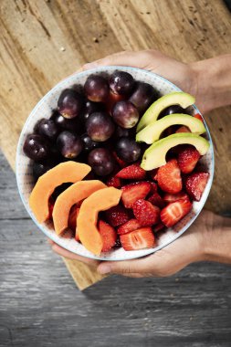 yüksek açılı görünüş avokado, papaya, çilek, üzüm ve yaban mersini, Doğrama tahtası üzerinde yapılan bir meyve salatası ile seramik kase sahip bir beyaz adam ahşap masanın üzerine yerleştirilen