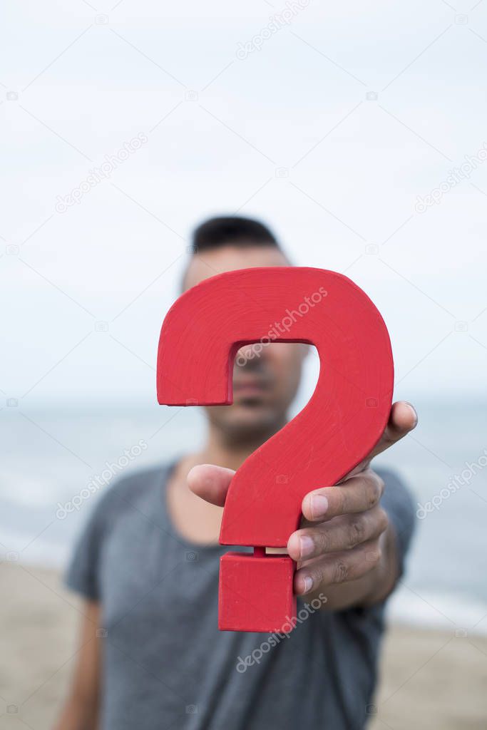 closeup of a young caucasian person with a question mark in front of her or his face, with the ocean in the background