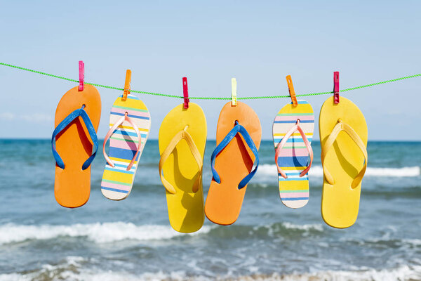 Крупный план некоторых различных пар красочных шлепанцев висит на линии одежды на пляже, с морем в фоновом режиме
