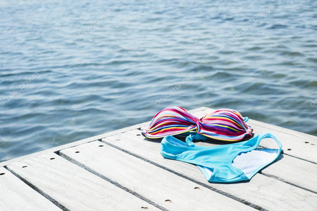 a colorful bikini drying on a wooden pier next to the water