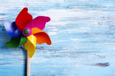 closeup of a colorful pinwheel, with the colors of the rainbow, on a blue rustic wooden background with some blank space on the right clipart