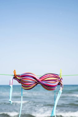 closeup of the colorful top of a bikini hanging on a clothes line on the beach, with the sea in the background, with a blank space on top clipart
