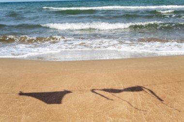 bir bikini bir elbise çizgi denizin içinde belgili tanımlık geçmiş ile bir plaj kum üzerinde asılı iki adet silüeti