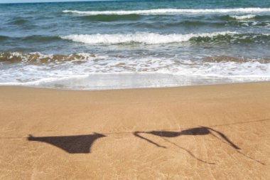 the silhouette of the two pieces of a bikini hanging on a clothes line on the sand of a beach, with the sea in the background clipart