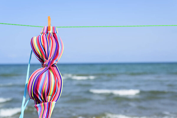 Крупный план красочной вершины бикини, висящей на линии одежды на пляже, с морем на заднем плане
