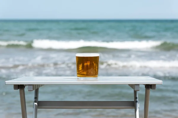 特写一杯清爽的啤酒在海滩上的户外餐桌上 与海洋背景 — 图库照片