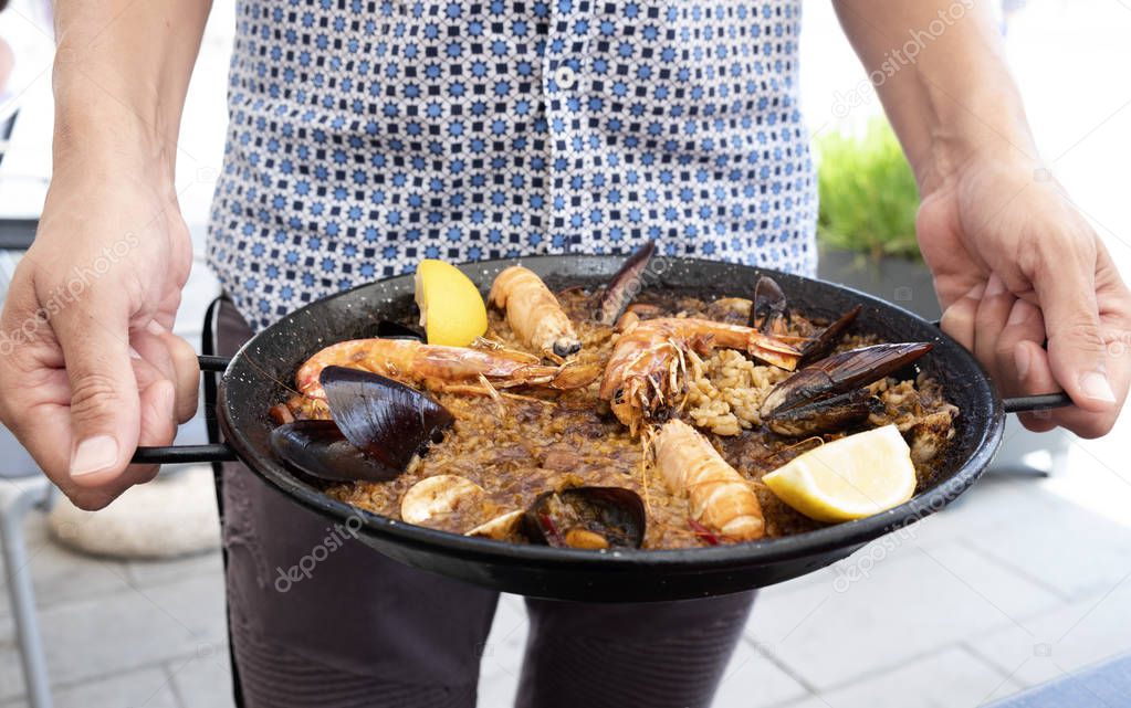 closeup of a young caucasian holding a typical spanish seafood paella in the paellera, the paella pan