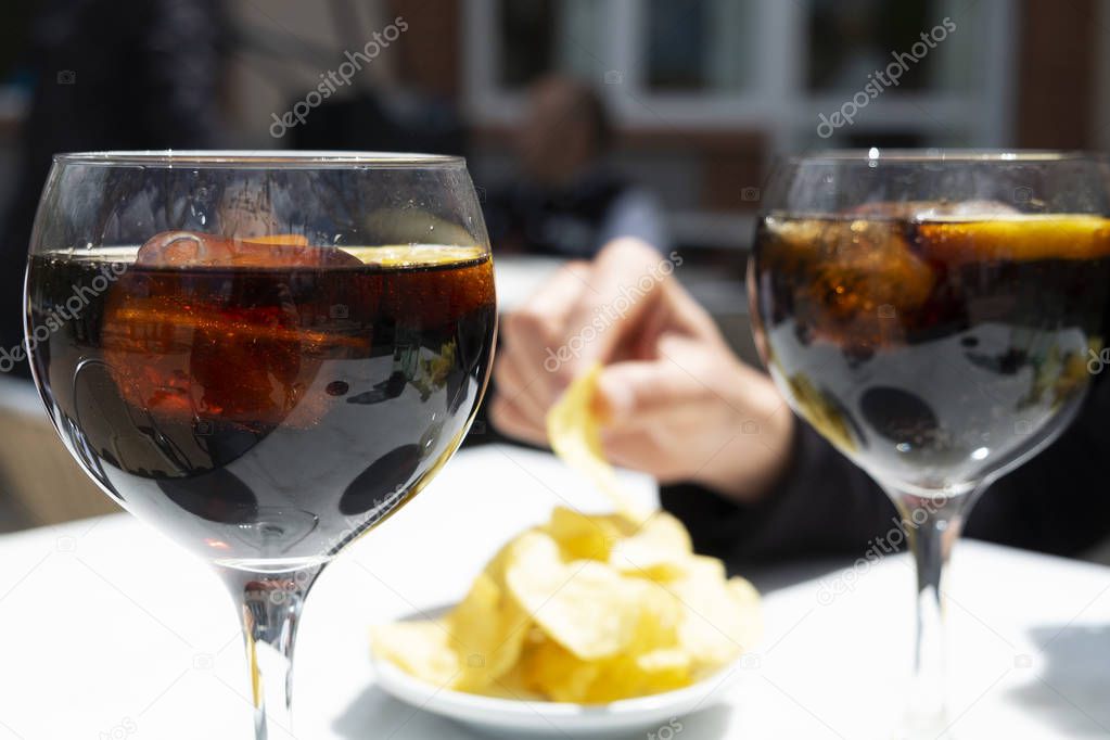 closeup of two glasses with vermouth, a fortified wine served on the rocks with a slice of orange, and a bowl with potato chips, eaten traditionally as an appetizer on Sundays in Catalonia, Spain