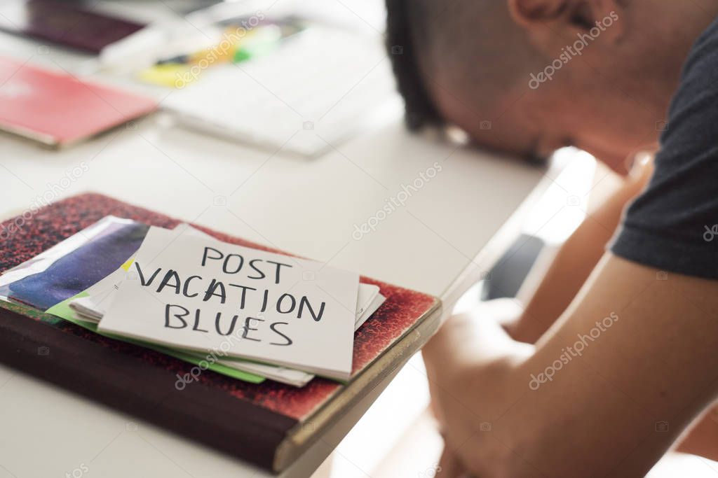 closeup of a concerned man sitting at his office desk and a note in the foreground with the text post-vacation blues handwritten in it