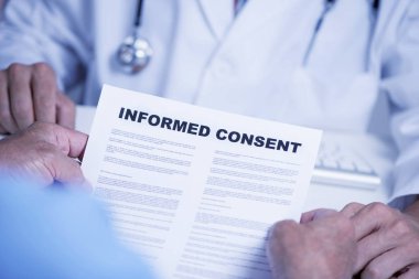 closeup of a senior caucasian man, at the doctors office, reading an informed consent document in front of a caucasian doctor man, in a white coat, sitting both at the doctors desk clipart