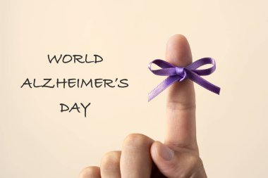 adam onun işaret parmağı ve metin Dünya Alzheimer günü bir off-beyaz arka plan üzerinde bağlı bir mor kurdele ile