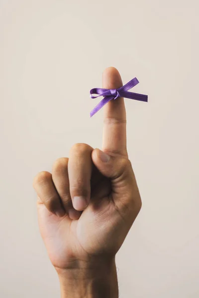 世界のアルツハイマー病日 オフホワイトの背景に彼の人差し指に縛ら紫リボンを持つ男 — ストック写真