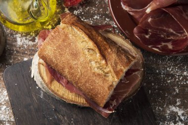 tipik İspanyol bocadillo de jamon serrano jambonlu sandviç, yüksek açılı görünüş rustik ahşap bir masa, bir plaka ile bazı dilim serrano jambonu ve zeytinyağı ile bir cruet yanında tarih