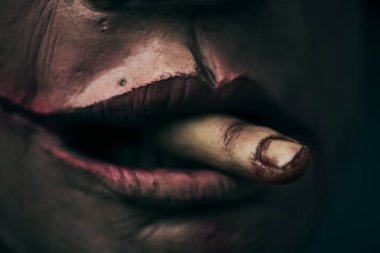 closeup of a scary disfigured man with a bloody amputated finger emerging from his mouth clipart
