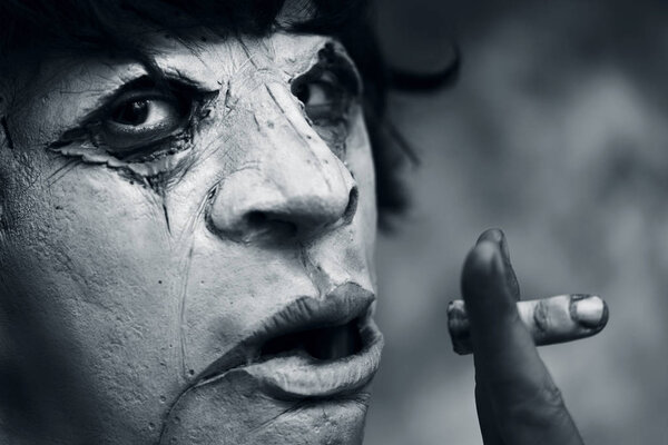 closeup of a scary disfigured man holding a bloody amputated finger between his fingers, as he was smoking, in black and white