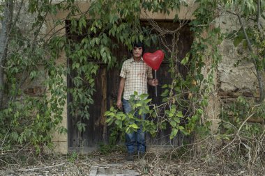 korkutucu bir kirli giyen adam, sakat ve kalp şeklinde balon terk edilmiş bir evde kapı önünde otlar tarafından örtülü bir kırmızı elbise hizalayıp düzensiz bırakmak
