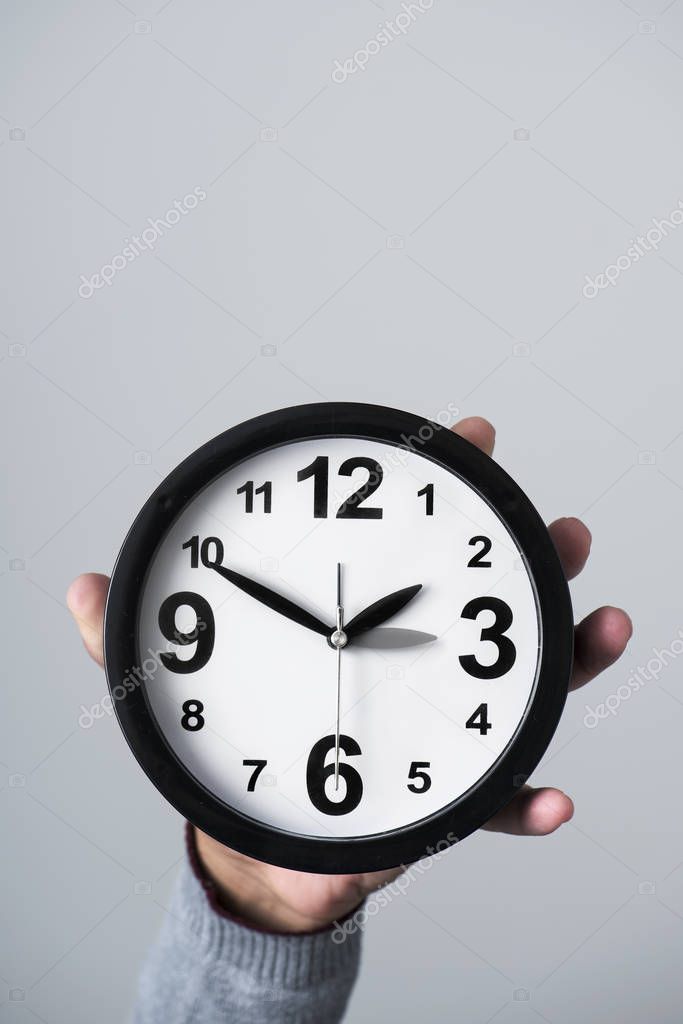 closeup of the hand of a young caucasian man holding a clock which is being adjusted backward or forward one hour at the end or at the beginning of the summer