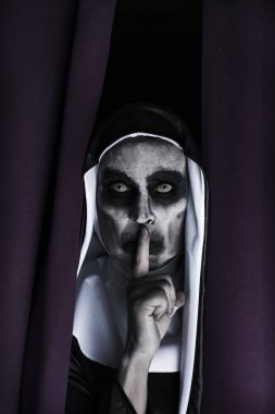 closeup of a frightening evil nun, wearing a typical black and white habit, peeping out from a purple curtain, asking for silence clipart