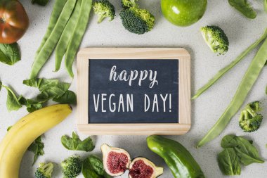 bir tabela metin mutlu vegan gün ve bazı farklı meyve ve çiğ sebze, bir yığın ile yüksek açılı görünüş bir beyaz taş tezgah üzerinde