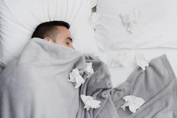在床上的一个生病的年轻白种人的高角度视图 覆盖着浅灰色毯子 被使用的组织包围 — 图库照片
