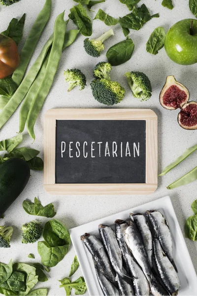 Vejetaryen insanlar balık ve bazı farklı meyve ve çiğ sebze, yemek için metin pescetarian ile bir tabela ve bir beyaz taş tezgah üzerinde bir tabak sardalya yığını