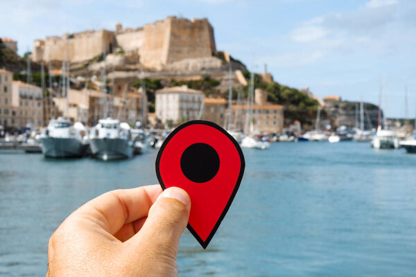 closeup of the hand of a caucasian man holding a red marker at the port of Bonifacio, in Corse, France, and its famous citadel in the background