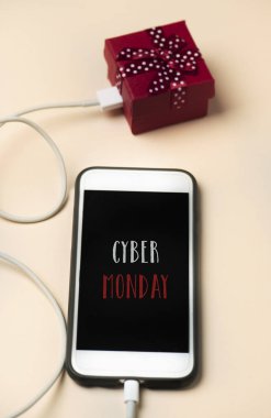 closeup bir smartphone ile metin mutlu cyber Pazartesi onun ekranında bir hediye için bir kablo ile bağlı, off-beyaz bir yüzeye yerleştirilir.