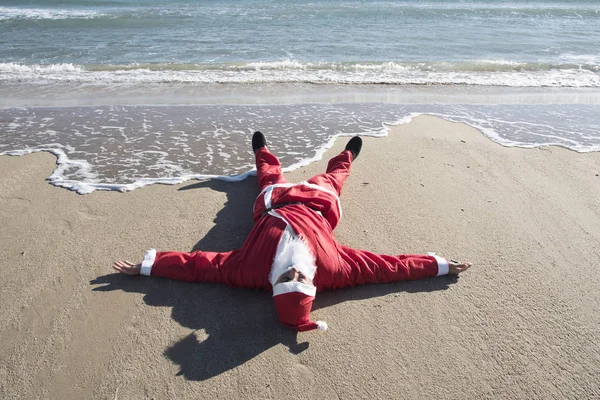 Santa Claus Leżącego Twarzą Góry Piaszczystej Plaży Morzem Tle — Zdjęcie stockowe