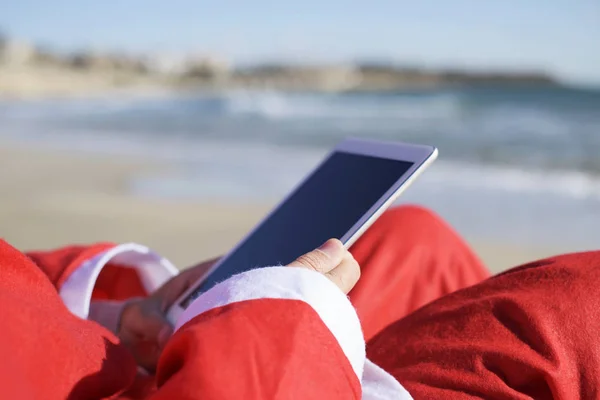Крупный План Санта Клауса Помощью Планшета Сидящего Пляже — стоковое фото